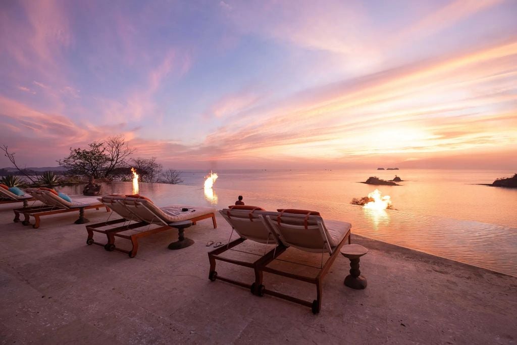 Elegant infinity pool overlooking lush Costa Rican jungle and Pacific Ocean at sunset, with modern lounge chairs and tropical landscaping