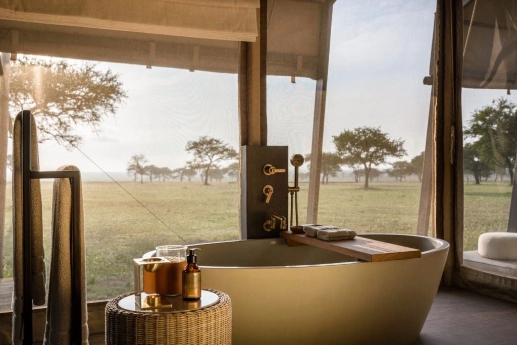 Luxurious safari tent with canvas walls, wooden deck, and designer furniture overlooking vast golden Serengeti grasslands at sunset