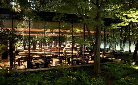 Modern Japanese hotel lobby with soaring stone walls, minimalist bamboo screens, and tranquil water feature beneath natural skylight