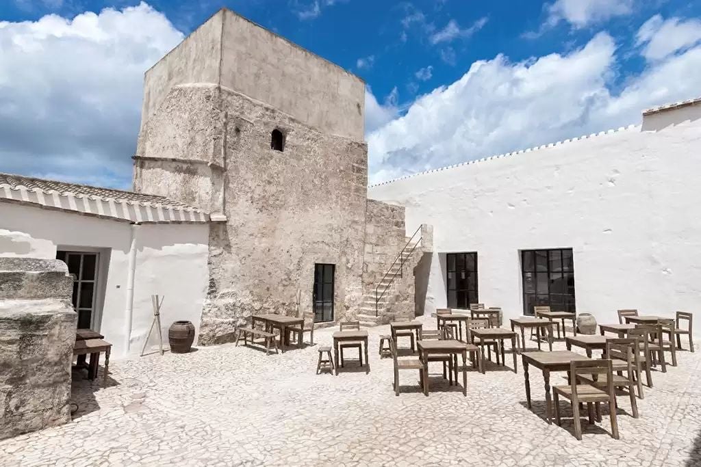 Historic stone tower hotel in scenset, Spain, with warm sunset hues illuminating stone walls, arched windows, and lush Mediterranean landscape surrounding luxurious stone architecture