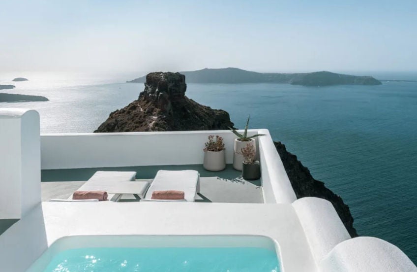 Modern hotel suite with private plunge pool overlooking Santorini caldera, featuring whitewashed walls and traditional Cycladic architecture