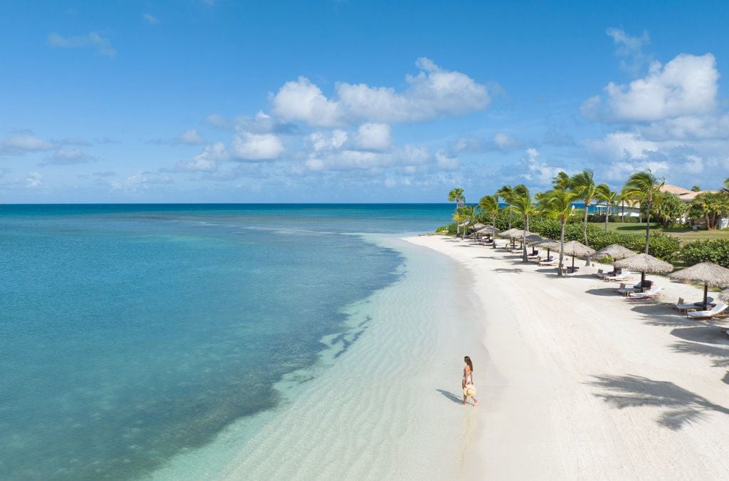 Luxurious beachfront resort on a pristine Caribbean island, white sandy beach, turquoise waters, and lush tropical vegetation surrounding elegant resort buildings.