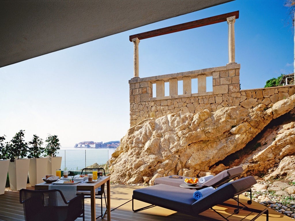 Modern cliffside luxury hotel with glass balconies overlooking the Adriatic Sea, white exterior blends into rocky coastline of Dubrovnik