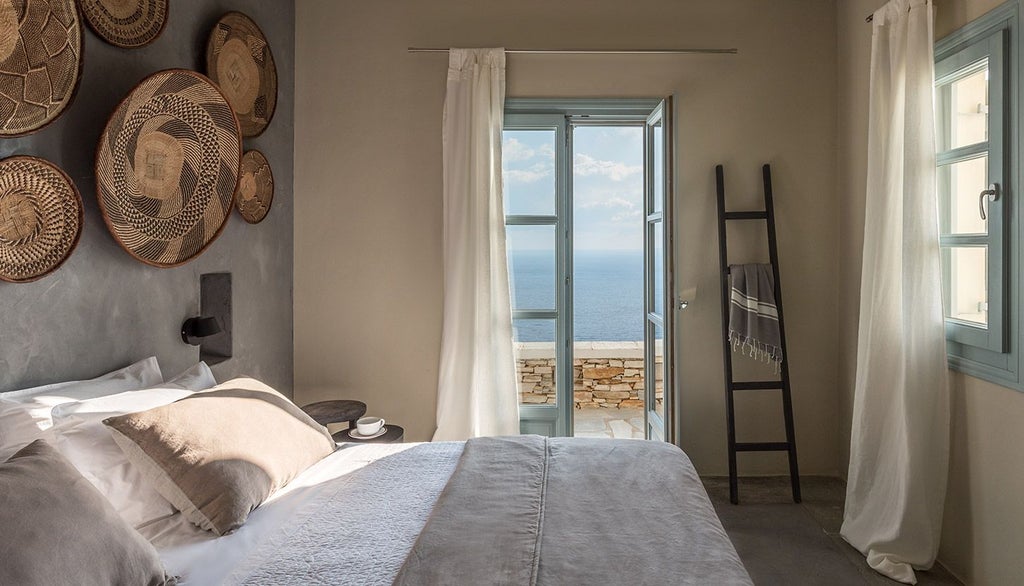 Luxurious minimalist hotel room with white marble floors, crisp white linens, and panoramic Aegean Sea view from Verina Astra in Sifnos, Greece