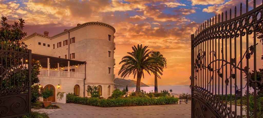 Elegant waterfront villa with white stone facade and red-tiled roof overlooking the Adriatic Sea, surrounded by lavender gardens.