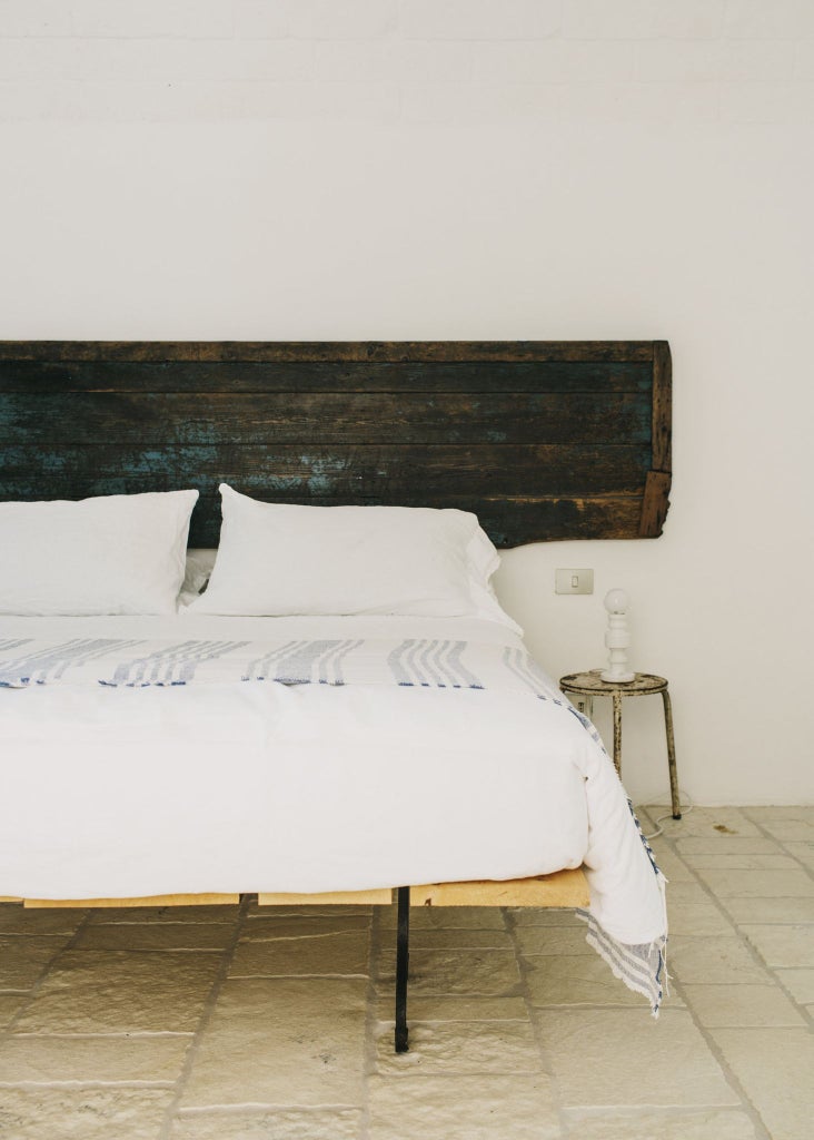 Minimalist white stone walls, rustic wooden furniture, and natural light illuminate a serene classic room at Masseria Moroseta's elegant countryside retreat in Puglia, Italy.