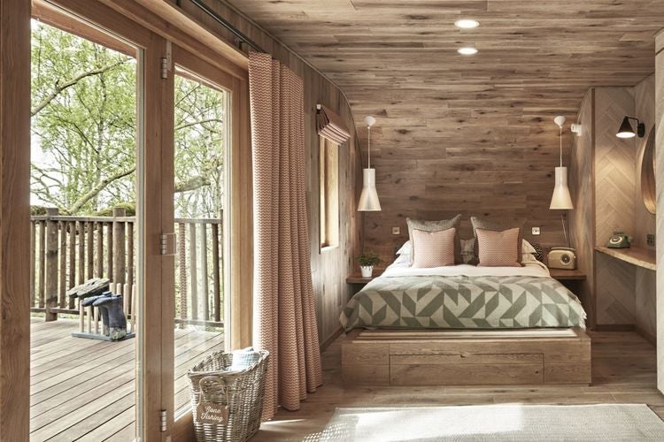 Modern treehouse-style hotel room with large windows overlooking lush forest, featuring minimalist wooden furnishings and a contemporary, nature-inspired luxury design