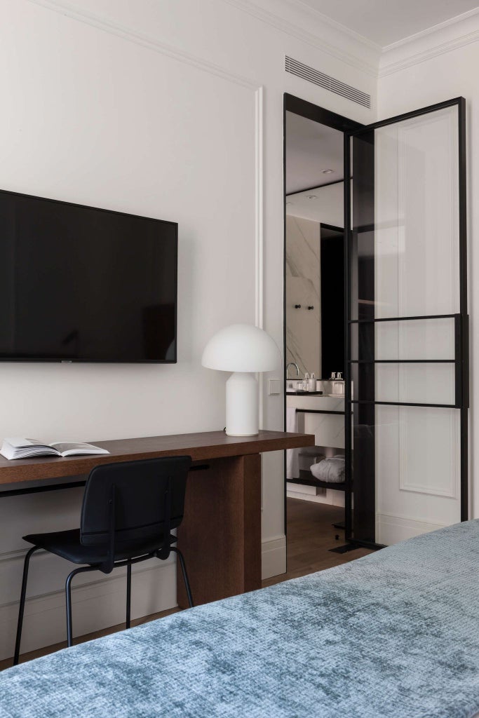 Elegant standard hotel room with modern minimalist design, crisp white linens, sleek furniture, and large window overlooking urban Budapest landscape