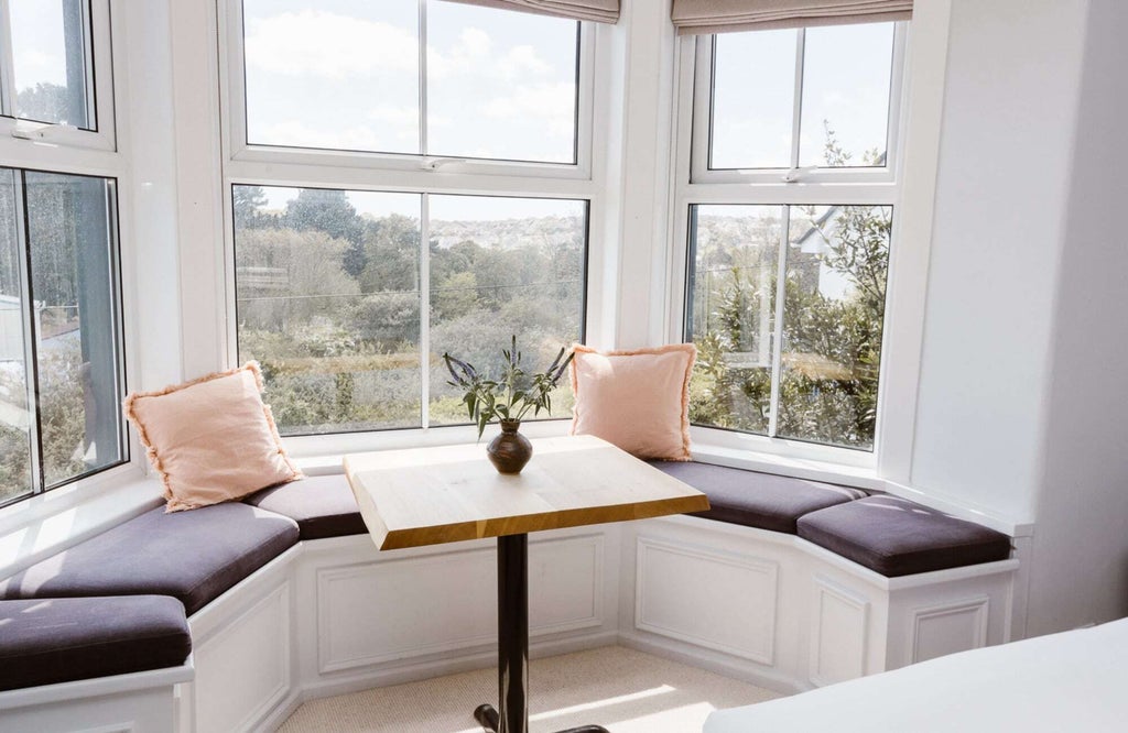 Elegant hotel bedroom with crisp white linens, plush cushions, wooden flooring, and soft neutral tones in a charming UK coastal accommodation