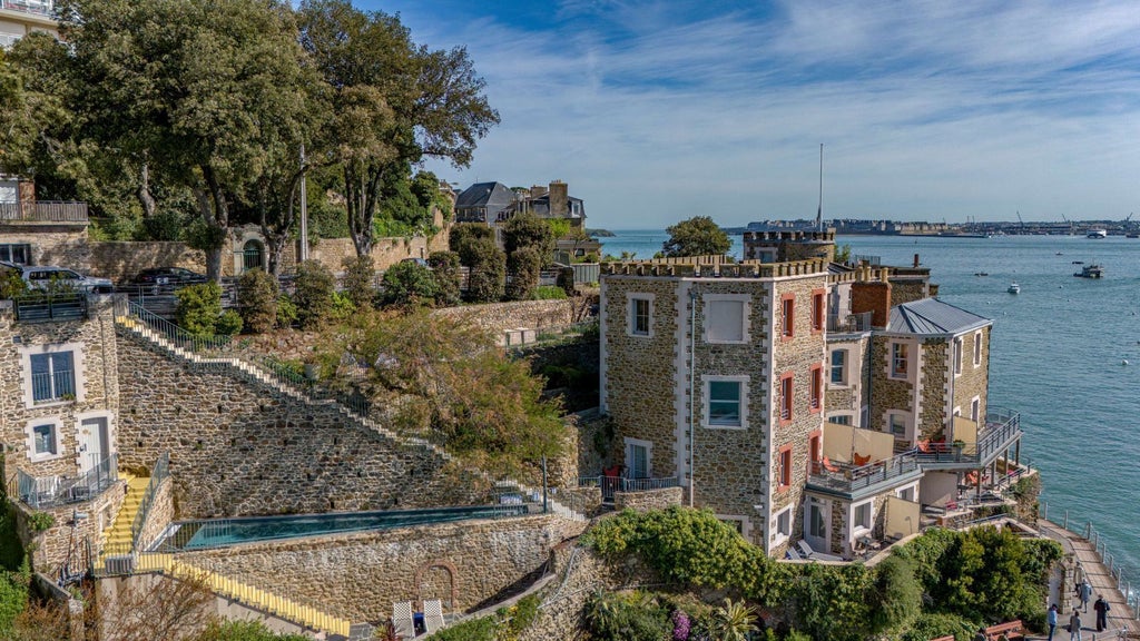 Luxurious coastal hotel overlooking rocky Brittany shoreline, featuring elegant blue-gray stone facade and pristine white trimmed windows