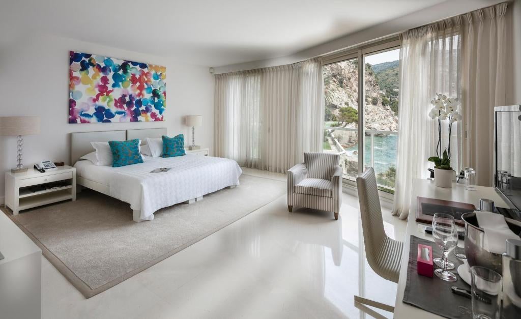 Luxurious seaside hotel built into cliffside with private Mediterranean beach, infinity pool, and terraced gardens at sunset