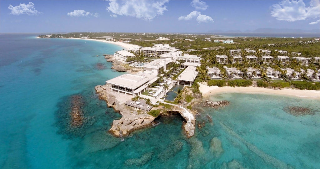 Luxurious oceanfront resort with infinity pools overlooking turquoise Caribbean waters, modern white architecture, and swaying palm trees