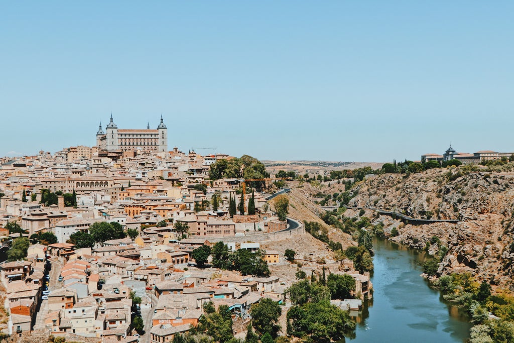 Panoramic view of Toledo's medieval skyline with golden sunlight illuminating historic stone walls, Gothic cathedral, and ancient cobblestone streets