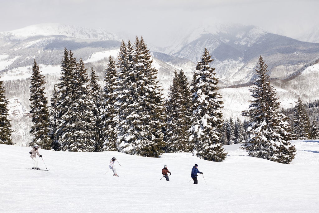 Luxurious mountain resort Four Seasons Vail features stone and timber facade, snow-covered peaks backdrop, and elegant outdoor terrace