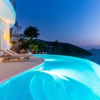 Luxurious cliff-side boutique hotel overlooking azure Mediterranean waters, white-washed architecture blending seamlessly with rugged Turkish coastline at sunset