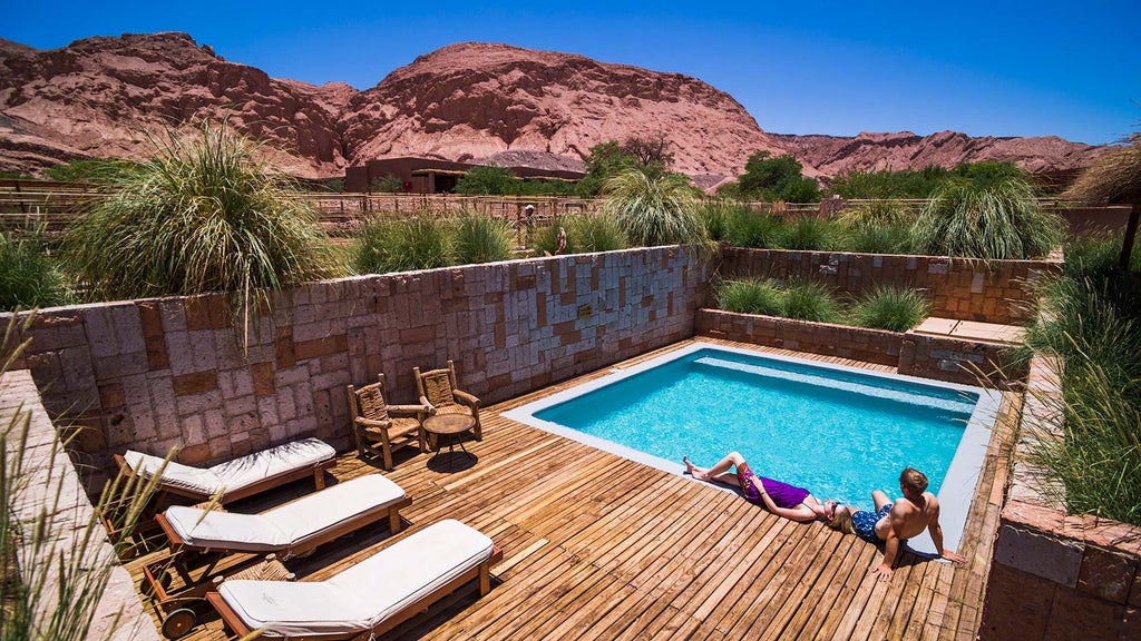 Desert lodge nestled in red rock canyon with sleek adobe architecture, infinity pool reflecting mountain peaks, terrace loungers at sunset