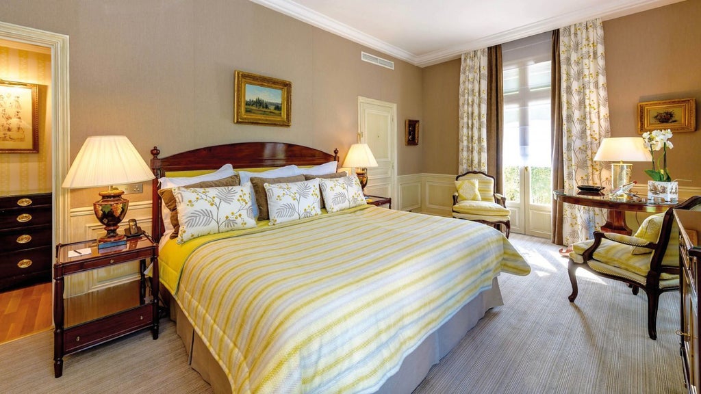 Classical French hotel room with ornate mirrors, crystal chandelier, antique furniture, and satin-draped windows overlooking manicured gardens