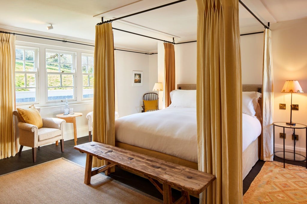 Elegant boutique hotel bedroom with soft cream walls, plush king-sized bed, antique wooden furniture, and delicate floral curtains in a luxurious UK countryside setting