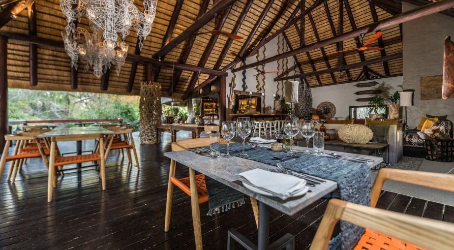 Elegant African safari lodge with thatched roof and wooden deck overlooking a serene river, surrounded by lush bushveld vegetation