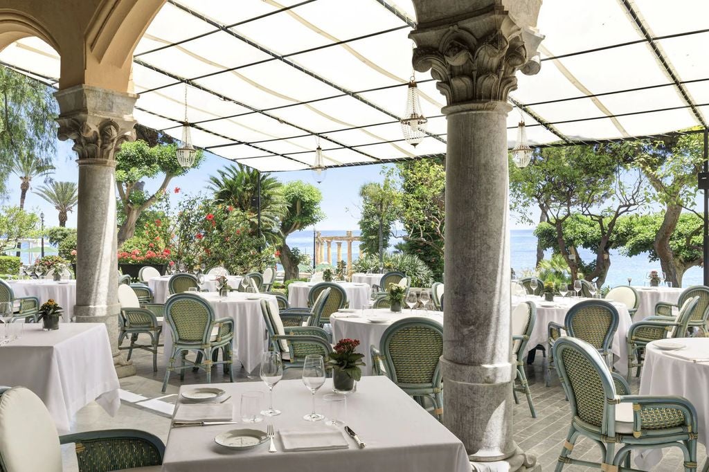 Elegant Mediterranean villa hotel with whitewashed walls, ornate balconies and lush gardens overlooking the Palermo coastline at sunset