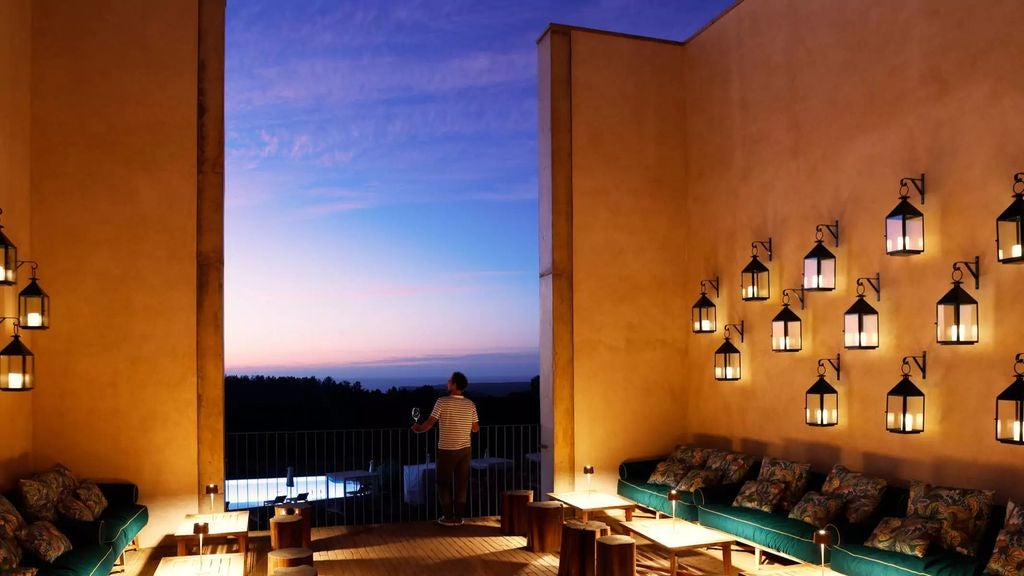 Elegant beachfront hotel with curved glass facade, infinity pool overlooking Atlantic Ocean, and palm-lined terrace at sunset