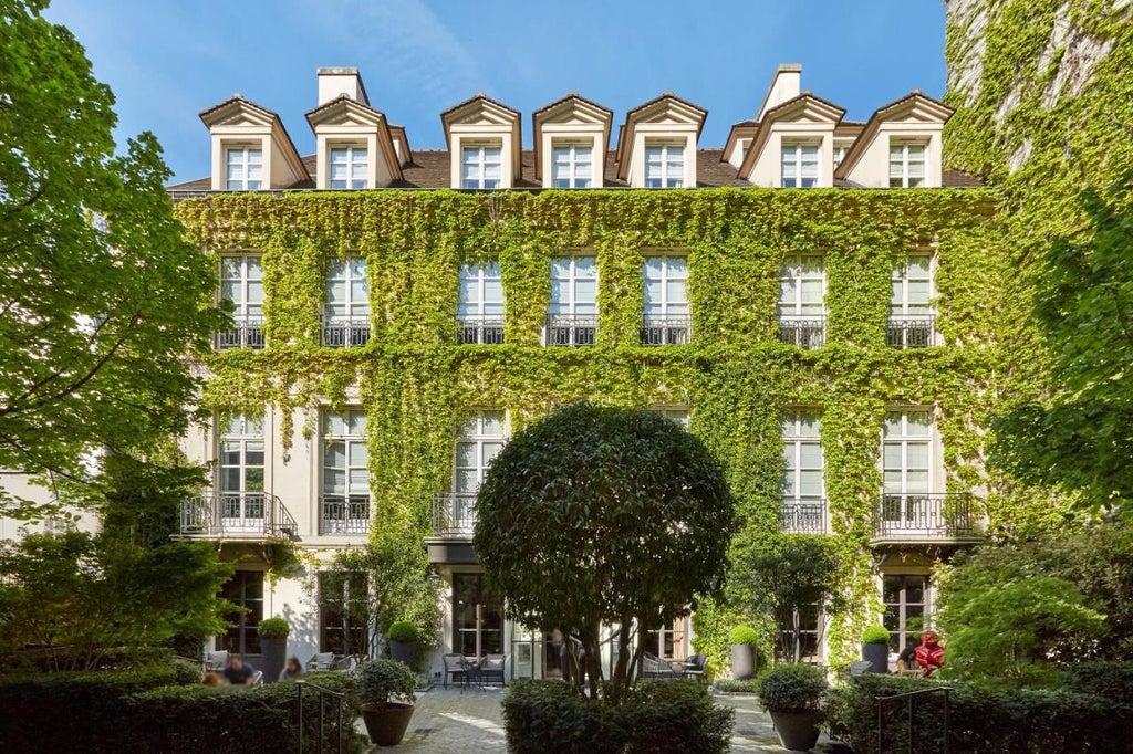 Elegant boutique hotel entrance with ivy-covered stone facade, wrought iron gates, and classic Parisian architecture in Le Marais district