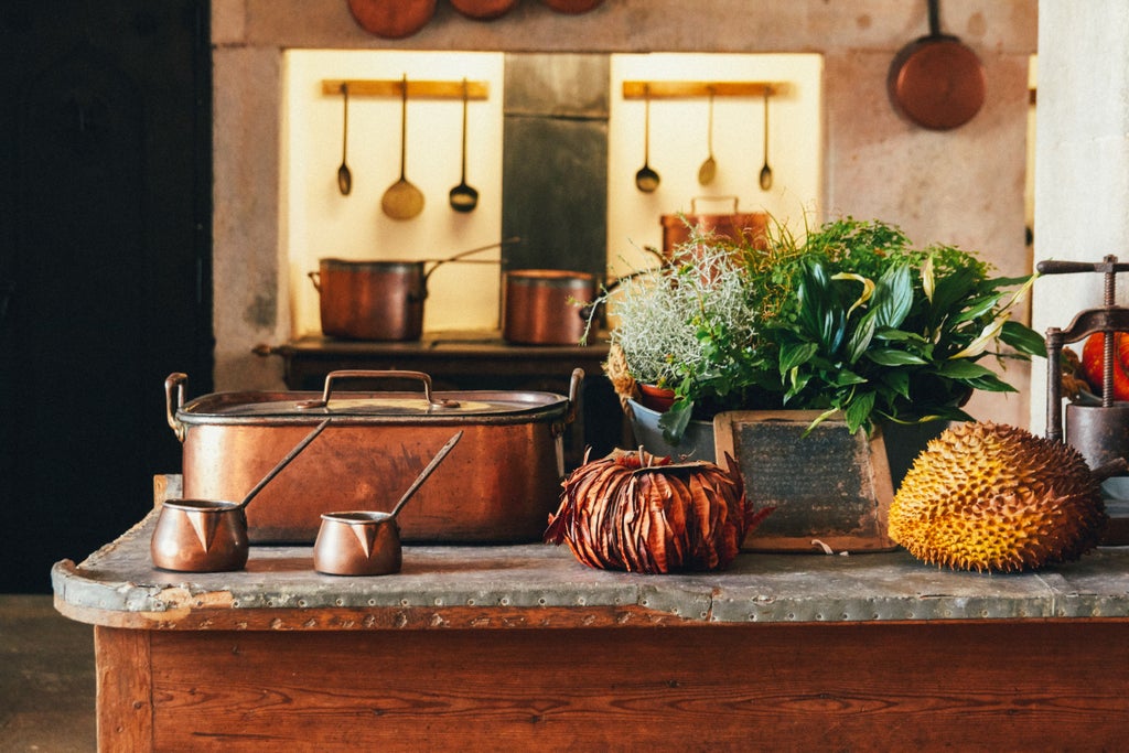 Sunlit Tuscan kitchen with marble counters, fresh ingredients, and copper cookware, overlooking Volterra's historic terracotta rooftops