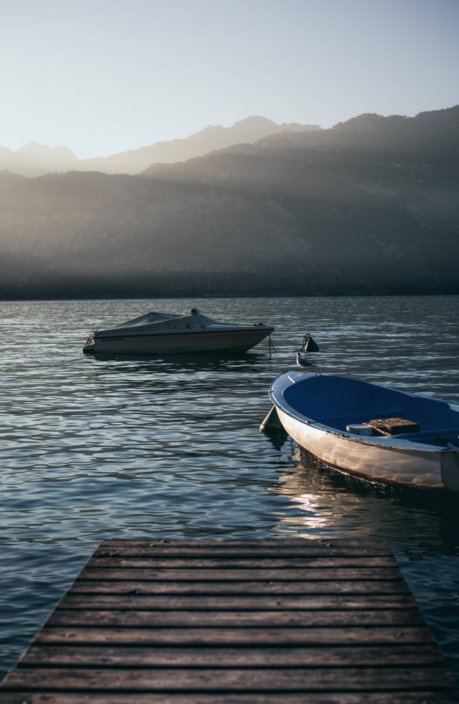 Stunning Lake Garda sunset with luxury sailboats moored in tranquil harbor, framed by rugged Italian Alps and historic waterfront villas