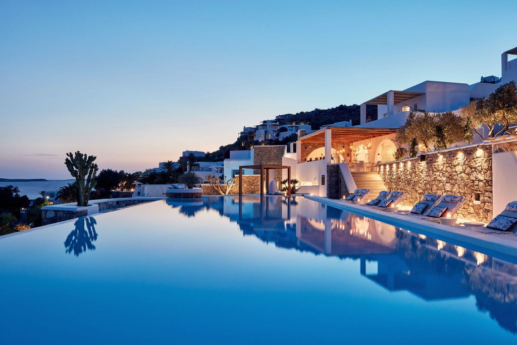 Luxurious white-washed Cycladic hotel with infinity pools overlooking azure Aegean Sea, perched on Santorini's dramatic volcanic cliffs at sunset