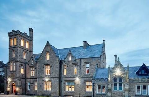 Elegant exterior of historic Scenset hotel with lush green parkland, Victorian architecture, warm lighting, and manicured gardens at dusk