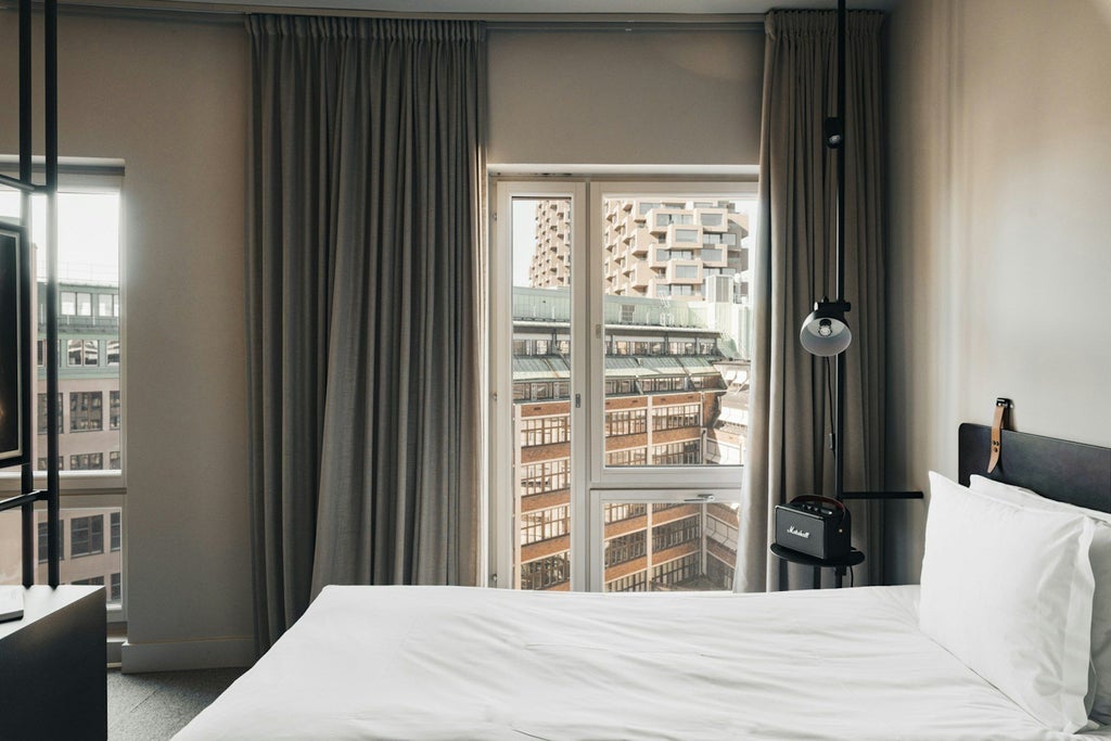 Modern Scandinavian hotel studio with minimalist design, crisp white bedding, sleek furniture, warm wood accents, and large window offering natural light and urban view