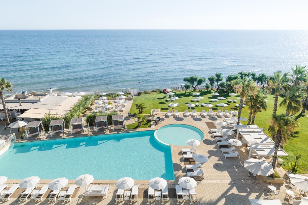 Elegant white luxury hotel nestled in coastal Italian landscape, showcasing minimalist architecture with lush greenery and sleek swimming pool design