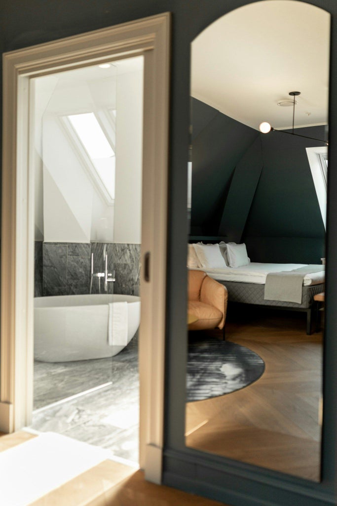 Modern, spacious junior suite with muted Nordic design, featuring elegant grey and white color palette, minimalist furniture, and large windows overlooking cityscape at scenset Hotel Copenhagen