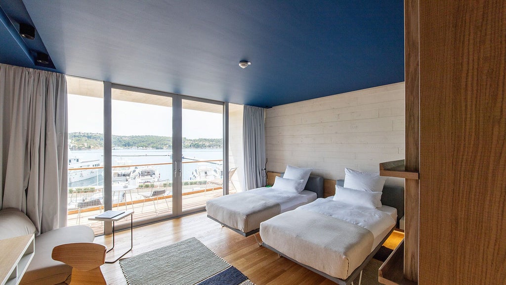 Spacious deluxe hotel room at D-Resort Šibenik with modern minimalist design, large windows, neutral color palette, and elegant sea-inspired decor