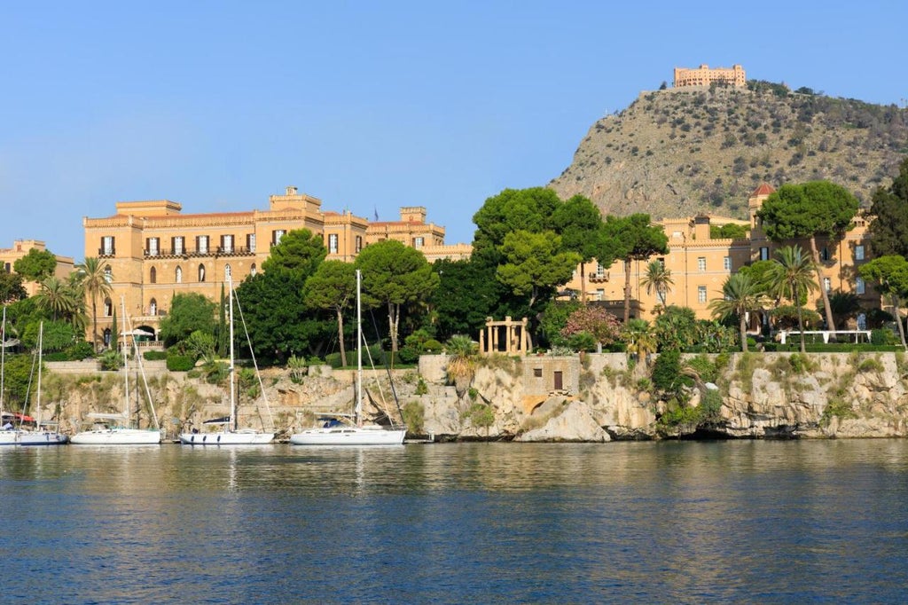 Historic Mediterranean villa with grand marble columns, manicured gardens and waterfront terrace overlooking Palermo's scenic coastline