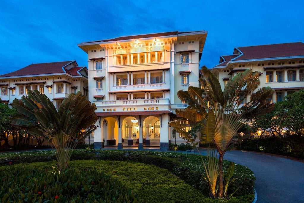 Elegant colonial-style facade of Raffles Hotel Cambodia, with white pillars, french doors, and lush tropical gardens framing the entrance