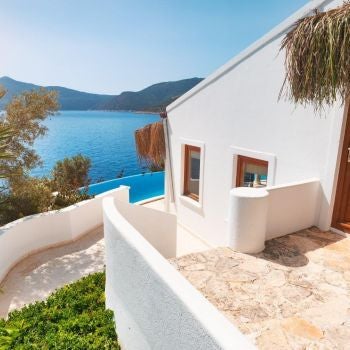 Elegant Turkish hotel room with white linens, wooden furniture, plush bedding, and large windows overlooking scenic landscapes at Villa Mahal resort