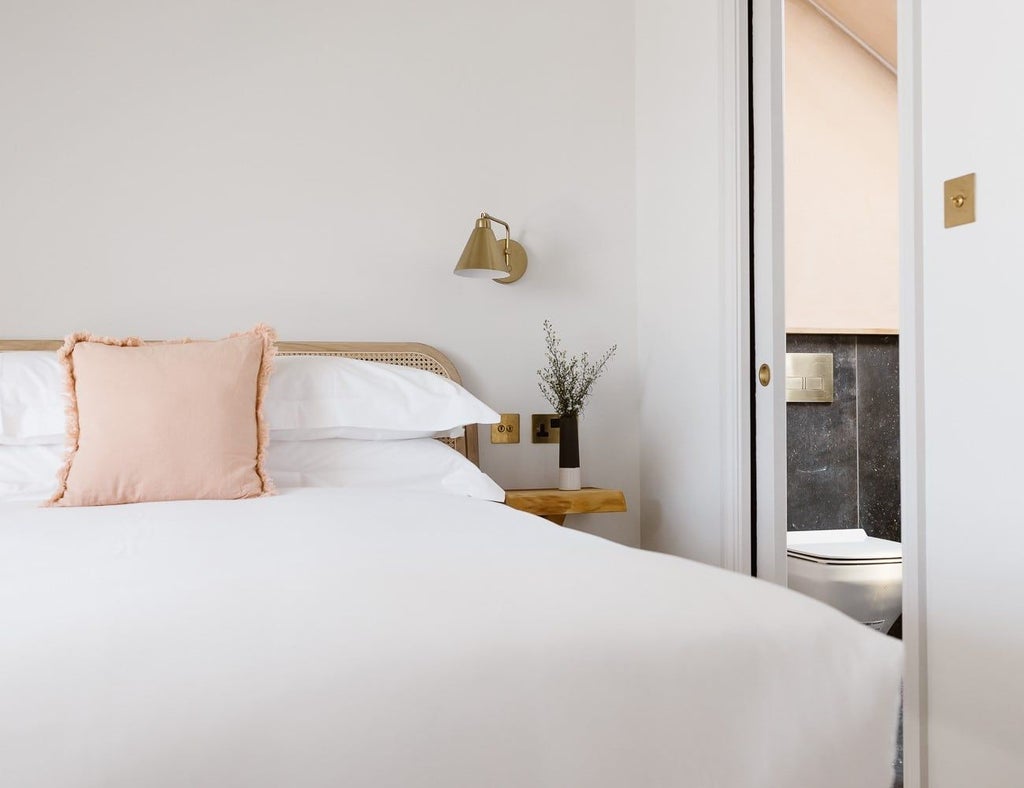 Elegant coastal bedroom with plush white bedding, soft blue accent walls, seaside-inspired artwork, and panoramic window overlooking tranquil scenery at The Sandy Duck hotel