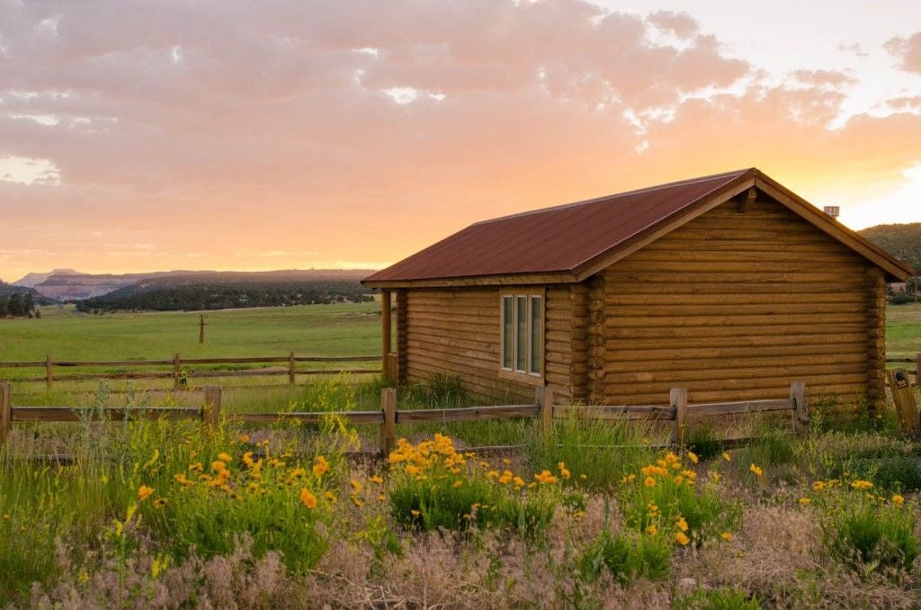 Rustic wooden cabin bedroom with plush bed, large windows overlooking scenic mountain landscape at Scenset Mountain Ranch in scenic western United States