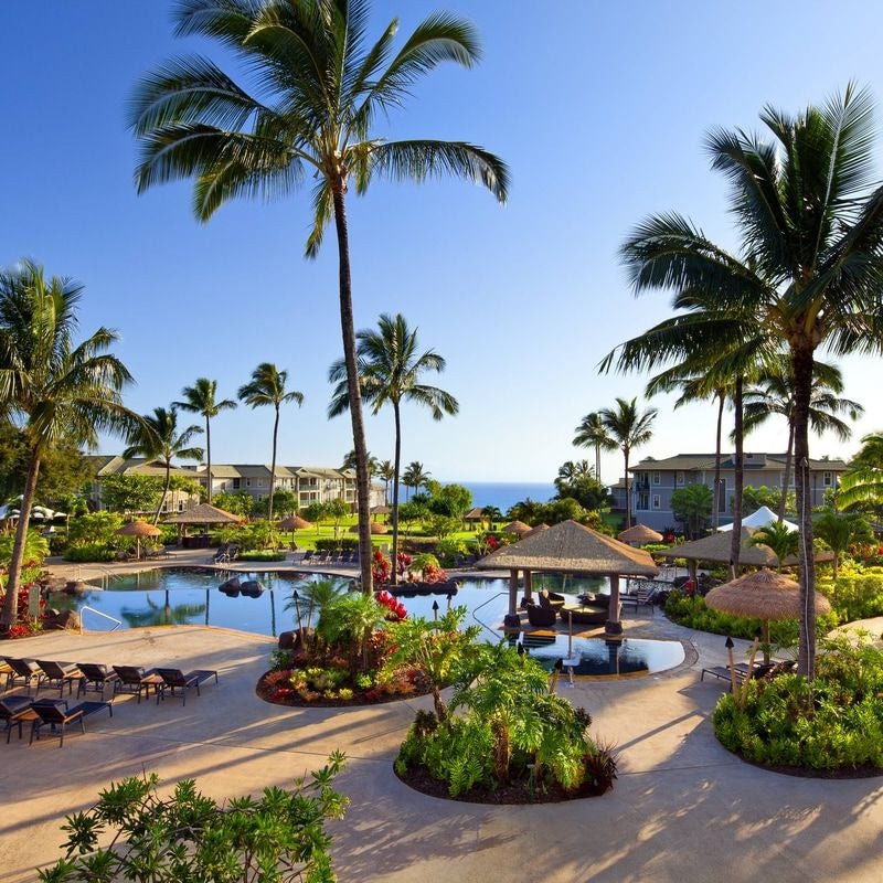 Luxurious oceanfront resort in Hawaii with multi-story white buildings, tropical landscaping, and infinity pools overlooking Pacific cliffs.