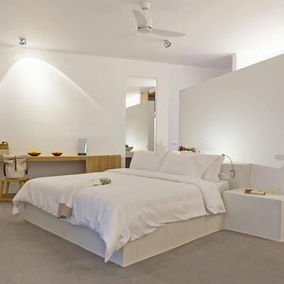 Elegant white-washed Santorini suite with sweeping Aegean views, minimalist design, private balcony, and plush king bed overlooking iconic blue-domed architecture