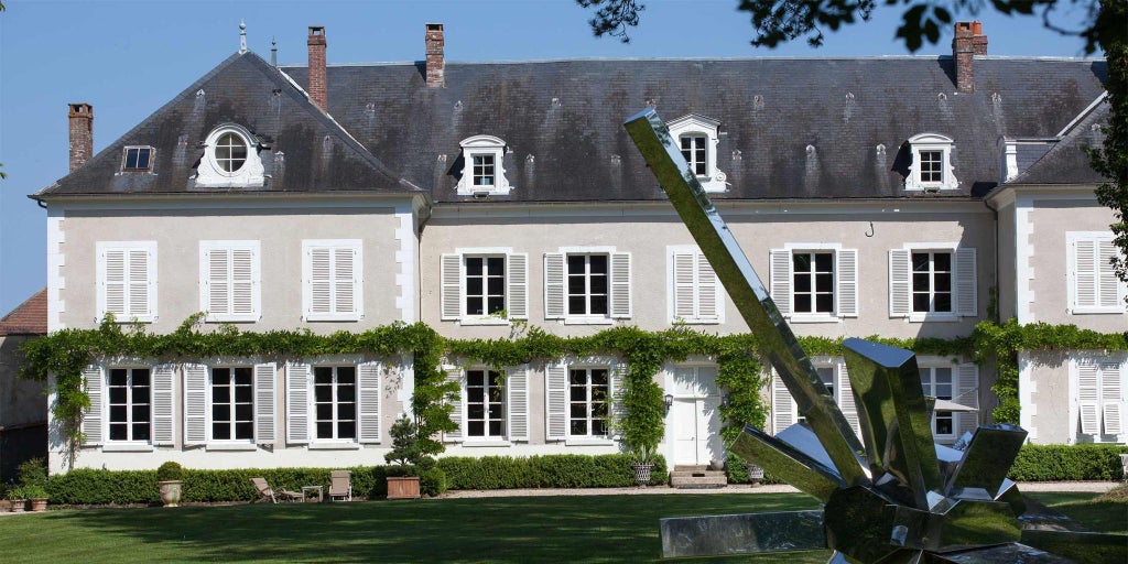 Luxurious minimalist hotel room with white walls, elegant furniture, and large windows overlooking the French countryside near Chablis.