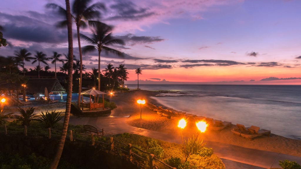 Oceanfront luxury resort with infinity pool merging into Pacific horizon, surrounded by palm trees and black lava rock formations