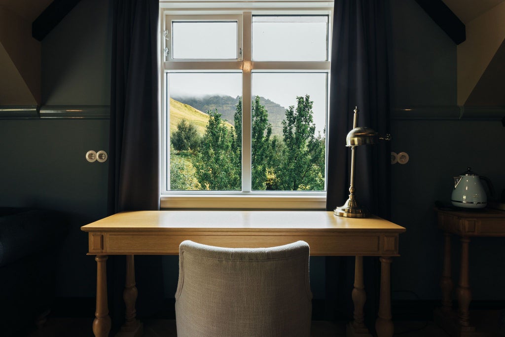 Luxurious grand room at Skálakot Manor Hotel with elegant wooden floors, plush white bedding, and panoramic Icelandic landscape views through large windows