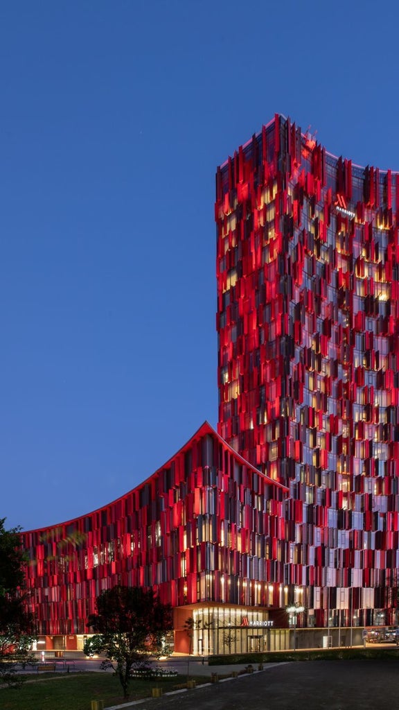 Elegant Tirana Marriott Hotel exterior at sunset showcasing modern glass facade, illuminated entrance and luxurious water feature