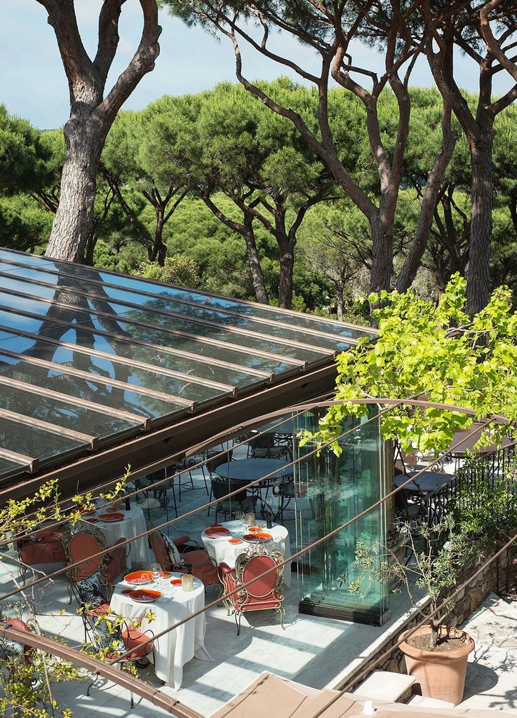 Elegant Mediterranean villa nestled in lush gardens, with white-washed walls, blue shutters, and terracotta roof overlooking Saint-Tropez coastline at sunset