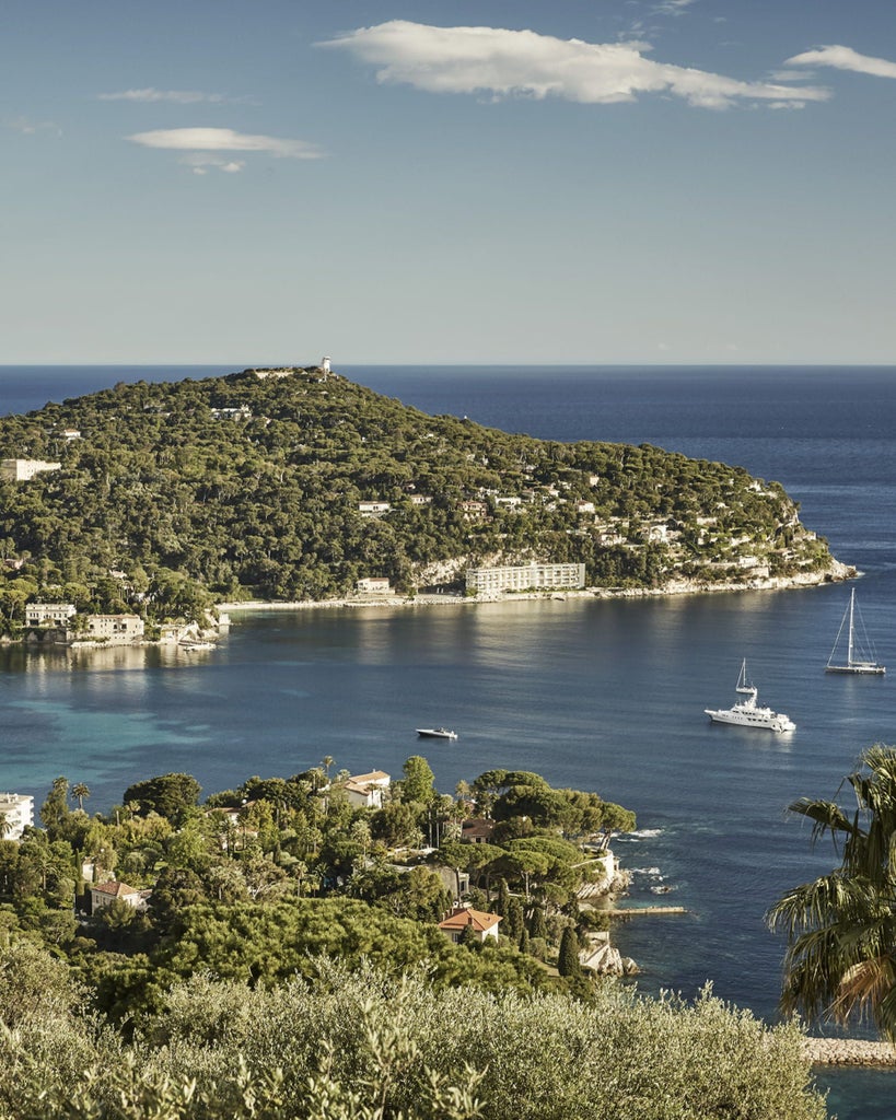 Elegant Mediterranean palace-style hotel with white facade, grand terraces and manicured gardens overlooking French Riviera coastline