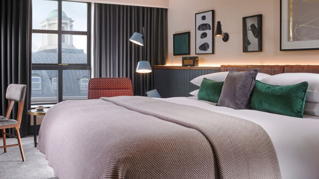 Elegant modern hotel room with plush white bedding, minimalist design, warm wood accents, and large window overlooking urban cityscape at the scenset Hotel in Ireland.