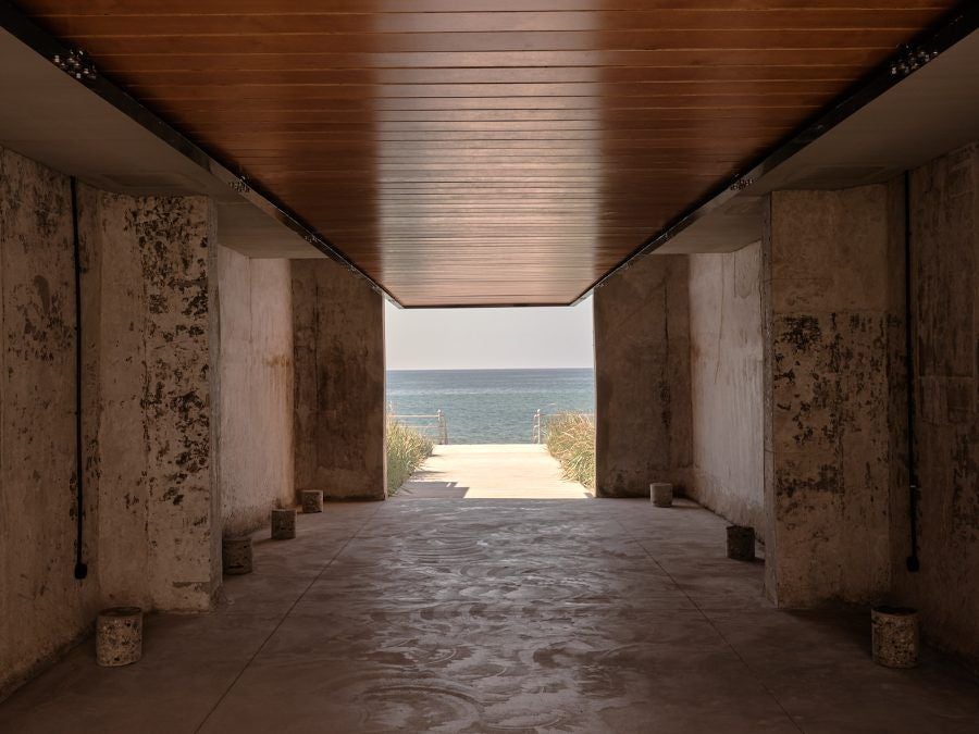 Minimalist concrete hotel nestled on Greek coastline, with sleek design blending industrial architecture and pristine azure Mediterranean waters