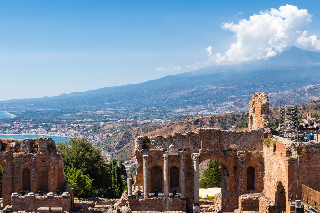 Tour guide leads visitors through charming cobblestone streets of Taormina, with ancient Greek Theater and Mount Etna in background